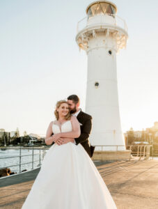 Bride and groom hugging in front of Wollongong Breakwater Lighthouse at sunset